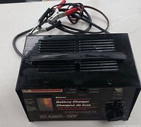 Photo of the top and cables of the Motomaster battery charger showing black casing, handle and attached cables with alligator clips.