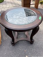 Front view showing circular wood coffee table with clear bevelled glass and carved leg details.