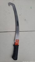 Side view of Schmidt pruning saw showing blade curvature, hooked tip, saw teeth, and black handle with orange securing piece.