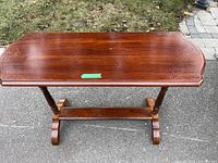 Side view of the wood side board table on an outdoor surface, showing decorative inlay detail and shape of the table top and supporting legs.