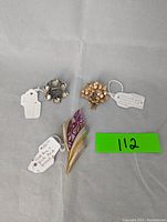 Photo showing three brooches laid flat on a grey background. The silver Solje brooch on the top left, floral pearl brooch on top right, and gold tone torch brooch on bottom center.