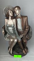 Full view of the art deco style statue showing a seated couple, man in bronze suit and woman in silver dress and hat.