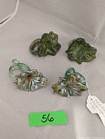 Four art glass leaf-shaped napkin rings on a neutral background with a green lot number tag.