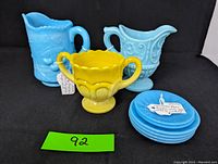 Lot overview showing blue milk glass creamers, yellow slag sugar bowl, and six mini plates
