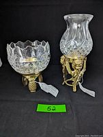 Pair of brass and crystal candle holders; left with pineapple brass base and scalloped crystal bowl, right with brass angels base and flared diamond-cut crystal shade.