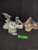 Four crystal and art glass figurines displayed on a black background: dolphin, cat, butterfly under dome, and art glass basket.