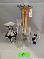 Lot of five vases against gray background including large iridescent spiral vase, floral porcelain vase, clear pressed and ribbed glass bud vases, and black and white glass cat bud vase.