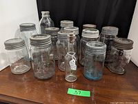 View of entire lot showing 13 mason fruit jars with metal lids, clear milk bottle, and Heinz Worcestershire bottle with glass stopper.