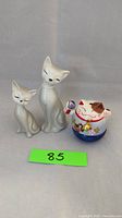 Front view of two gray Otogiri cat figurines and one colorful Japanese lucky cat figurine.