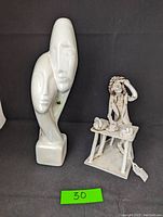 Two ceramic sculptures: the abstract cycladic couple statue and the seated office worker figure at a desk