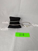 Three sterling silver bracelets displayed on and beside a black cushion: twisted bangle, patterned bangle, and abalone inlay Mexico bracelet.