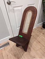 Full view of the vintage birthing chair showing its shape, solid wood construction, and woven backrest.