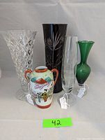 Photo showing all five vases in the lot including the ruby cut crystal vase, Kutani ware vase, green glass vase, etched glass vase, and clear crystal footed vase.
