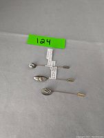 Three vintage sterling silver stick pins laid out on a flat surface with a bright green label '124'. Pins have decorative heads of abalone and blister pearl with metal caps on the backs.