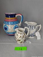 All three pitchers displayed together: colorful Wedgwood, antique Old Chelsea Furnivals, and large Bella Casa in blue and white dolphin motif.