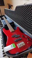 Red bass guitar seated in open hard shell case, view of body and case lining