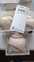Three signed baseballs in clear display cases. Close-up shows signatures on two of the balls, blue ink autographs visible.