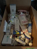 Box filled with assorted new unopened skin care and beauty products including lotion bottles, tubes, wipes, and small jars.