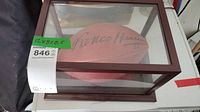 Football signed by Franco Harris inside a glass and wood framed display case with dimensions label attached.