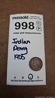Top-down photo of a 1905 Indian Head Penny on a MaxSold tag.