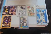 Photo of 7 trading cards laid out on table showing Kobe Bryant basketball cards, football cards including LaDainian Tomlinson, and baseball cards including Derek Jeter and Michael Jackson Dodgers
