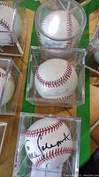 Three signed baseballs in protective cases on a green surface, one shows Barry Bonds signature