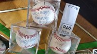 Photo showing three white baseballs in clear plastic display cases, each signed in blue ink.