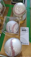 Three signed baseballs arranged with display cases, one on a round silver base, all showing signatures or inscriptions.