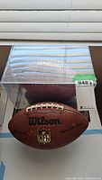 View of both footballs with the signed football inside a clear display case showing Wilson logo on top.