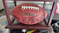 Frontal photo of the signed Wilson NFL football in its wood framed glass display case showing signatures and logos.
