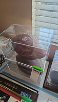 Two Wilson NFL footballs, each in clear display cases with visible signatures, placed on a white table near a window.