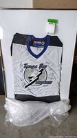 Full view of the framed Tampa Bay Lightning white hockey jersey with visible frame edges and protective plastic wrap at the base.