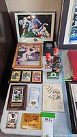 Full view of the lot showing framed photos, bobbleheads, trading card plaques, signed sheet, and sports pin grouped together on flat surface.
