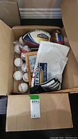 Photo showing box with white football, multiple baseballs, white towels and signed framed photo visible inside
