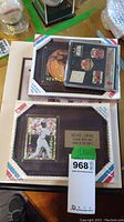 Two framed plaques sealed in original plastic packaging; one plaque prominently featuring a holographic Michael Jordan baseball card and a small brass plaque, other plaque box showing multiple sports memorabilia items including championship pins and basketball cards.