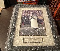 Framed photo of Drew Brees wrapped in bubble wrap with visible plaque.
