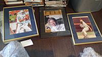 Framed sports photos featuring Dan Marino, Michelle McGann, and a baseball player, displayed together on a wooden floor