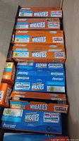 Photo of nine Wheaties cereal boxes stacked in a box, showing orange classic Wheaties and blue Honey Frosted Wheaties variants.
