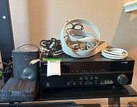 Front and top view of Yamaha receiver with coiled cables and one speaker visible, along with the black zippered case on the table.