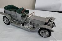 Side view showing silver body, green tufted seats, wooden steering wheel, detailed fenders and wheels.