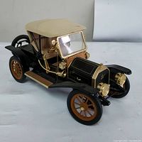 Front three-quarter view showing beige convertible top, black body, gold trim, and wood-colored wheels.