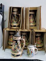 Seven ceramic beer steins shown. Six are large, boxed, lidded musical steins made in Japan, 10 inches tall. One smaller regular German beer stein in front.