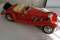 Side angle view of the red Burago Mercedes Benz 500K 1936 model showing beige interior and chrome details.