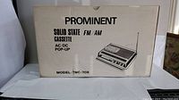 Box front showing brand Prominent, model TMC-70R, solid state FM/AM cassette radio, AC/DC pop-up.