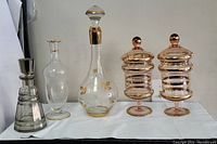 Photo showing all five decanters in a row, including the pink pair, tall white crystal decanter, grey crystal decanter, and the clear glass decanter
