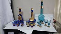 Three cobalt blue decorative shot glass sets with matching cobalt decanters, one additional green bottle, six blue and gold shot glasses including stemware.
