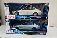 Two 1:18 scale Maisto BMW M5 model cars in their original packaging, one white and one silver, labeled special edition.