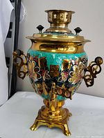 Front view of the samovar showcasing the brass body, hand-painted turquoise and gold floral design, and spigot.