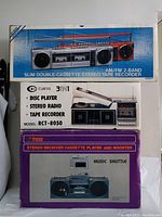 Three boxed vintage music devices stacked vertically: United slim double-cassette stereo tape recorder on top, Curtis 3-in-1 disc player/stereo radio/tape recorder in the middle, Prosonic stereo receiver cassette player and booster at bottom.