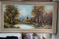 Full view of large framed oil painting showing the house by lake scene with trees and sky.